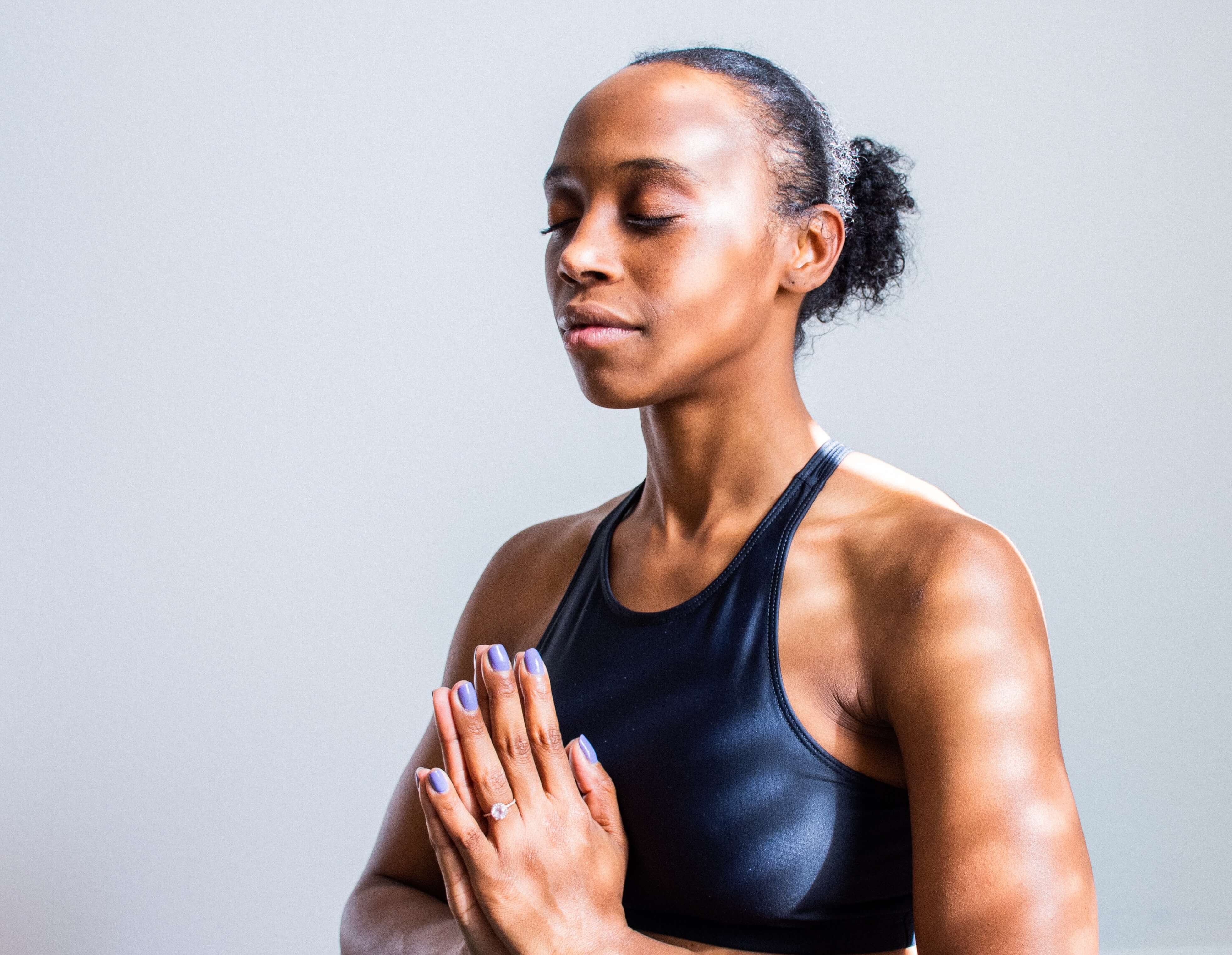 mujer negra sentada con las palmas juntas en el pecho meditando