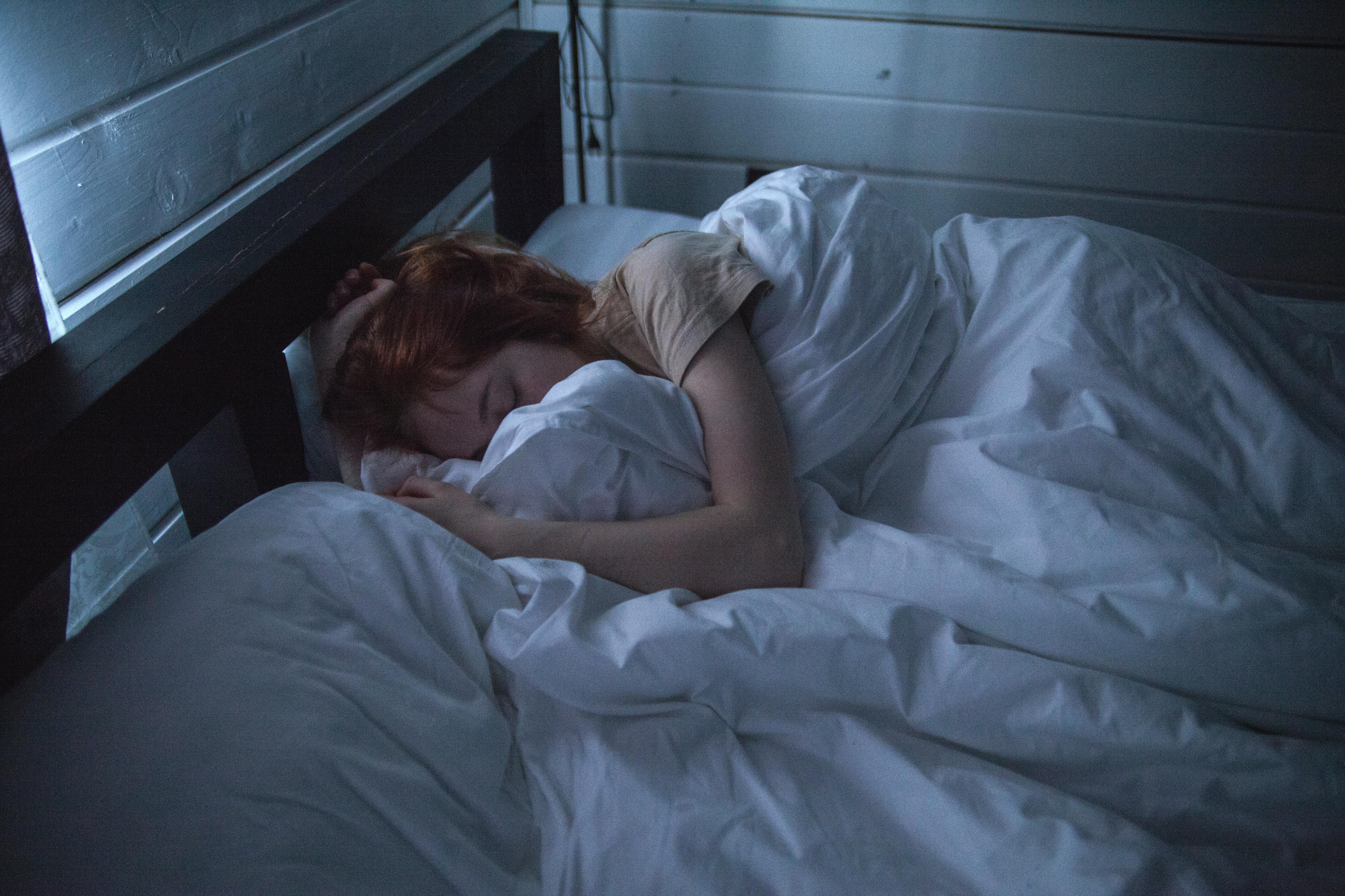 mujer durmiendo bajo una manta en una habitación oscura