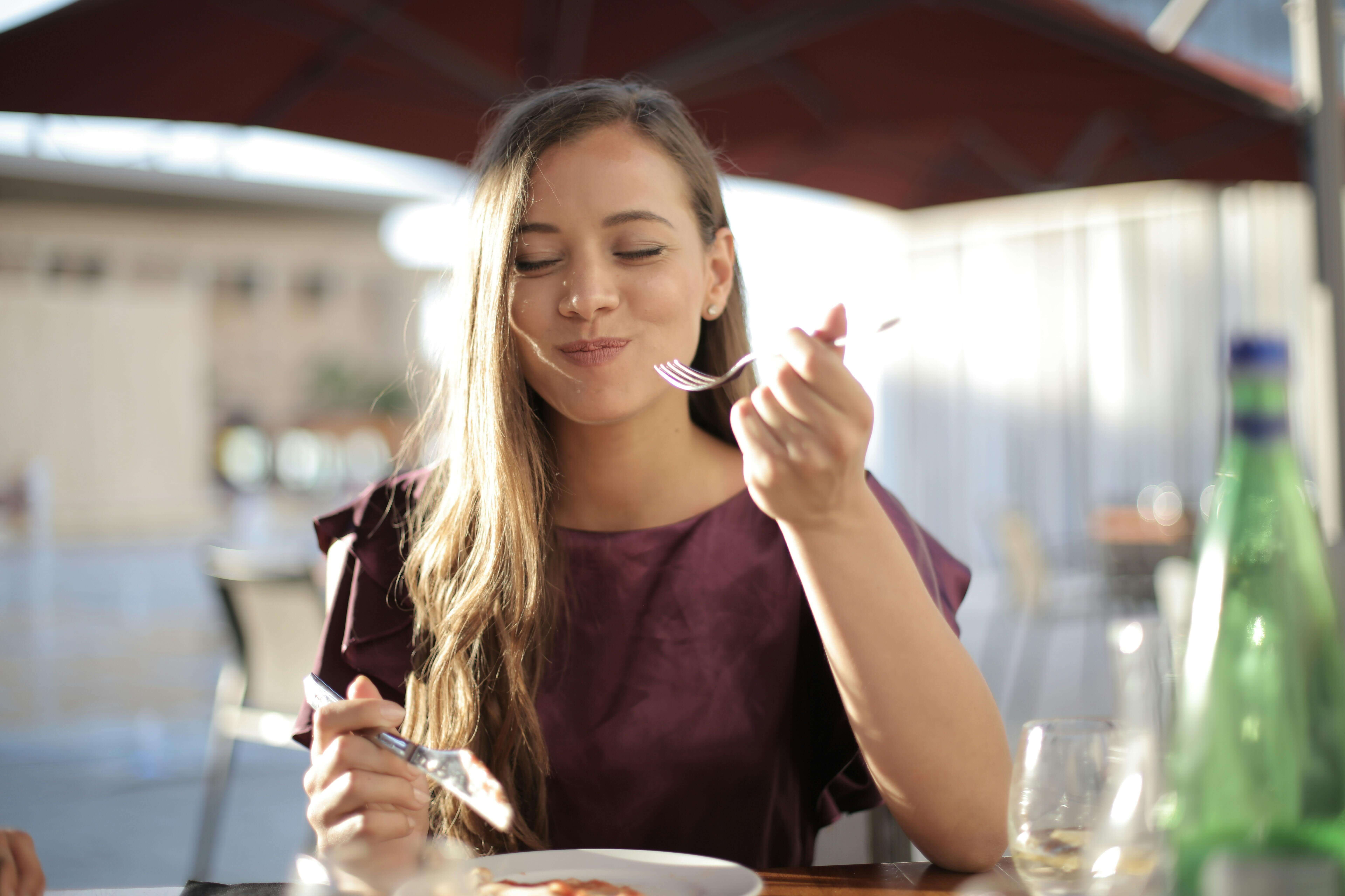 Mujer saboreando un bocado de comida y con aspecto alegre