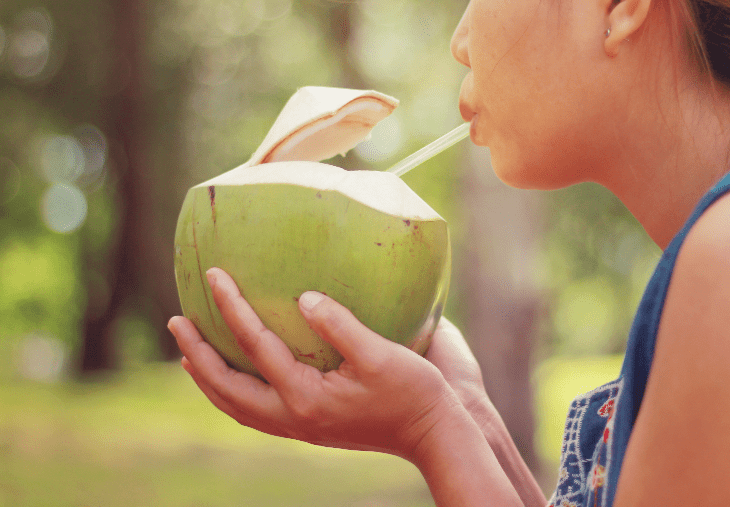 Mujer bebiendo agua de coco de un coco entero