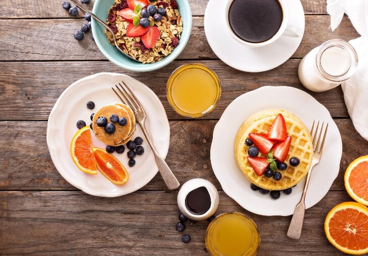 Vista aérea de alimentos para el desayuno, incluyendo granola, café, tortitas, sirope